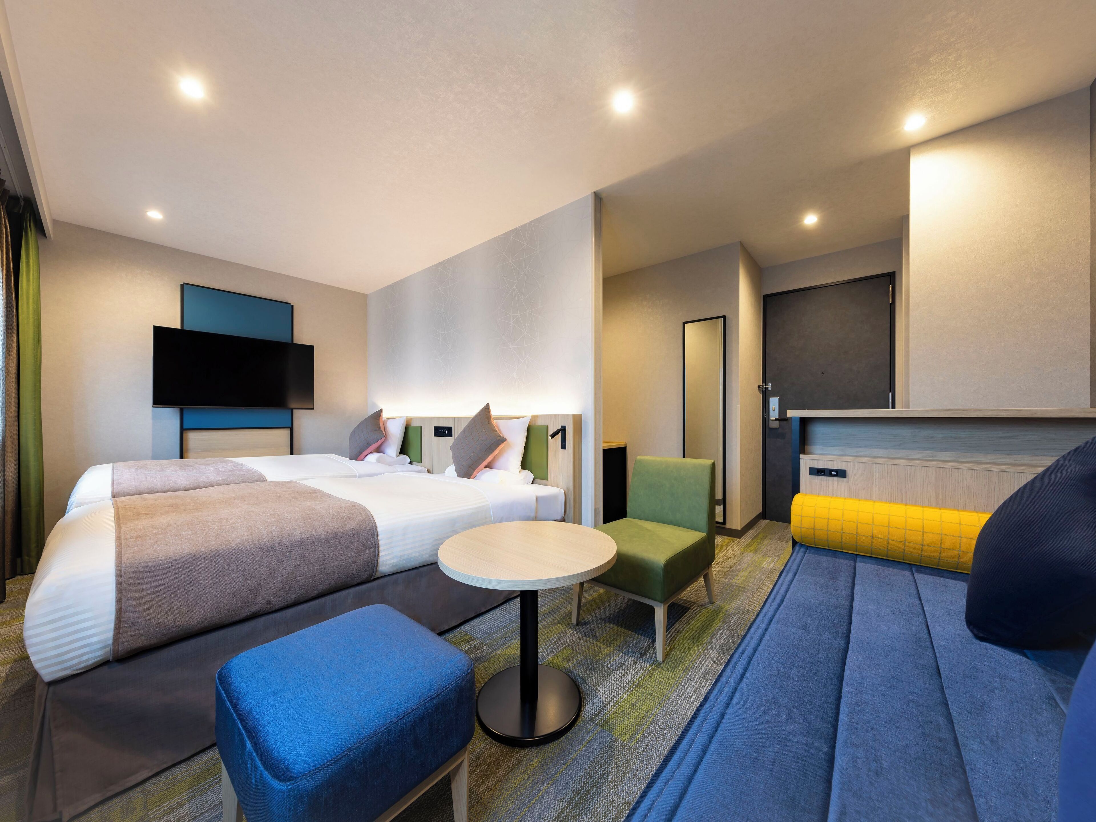 Une chambre d’hôtel moderne avec un grand lit, une petite table ronde, un canapé et un téléviseur fixé au mur.