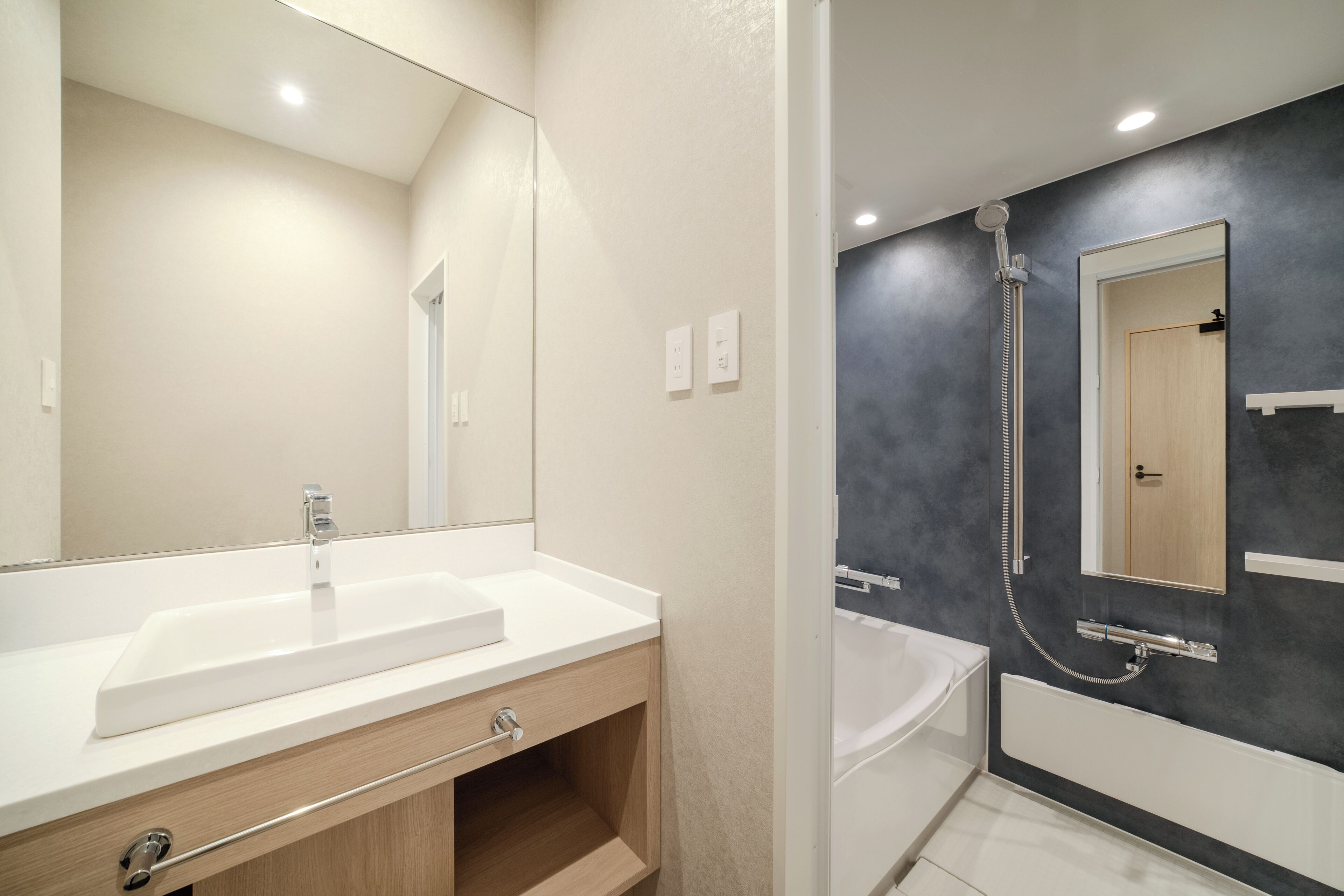 A modern bathroom with a large mirror, a white sink, a shower, and a bathtub.