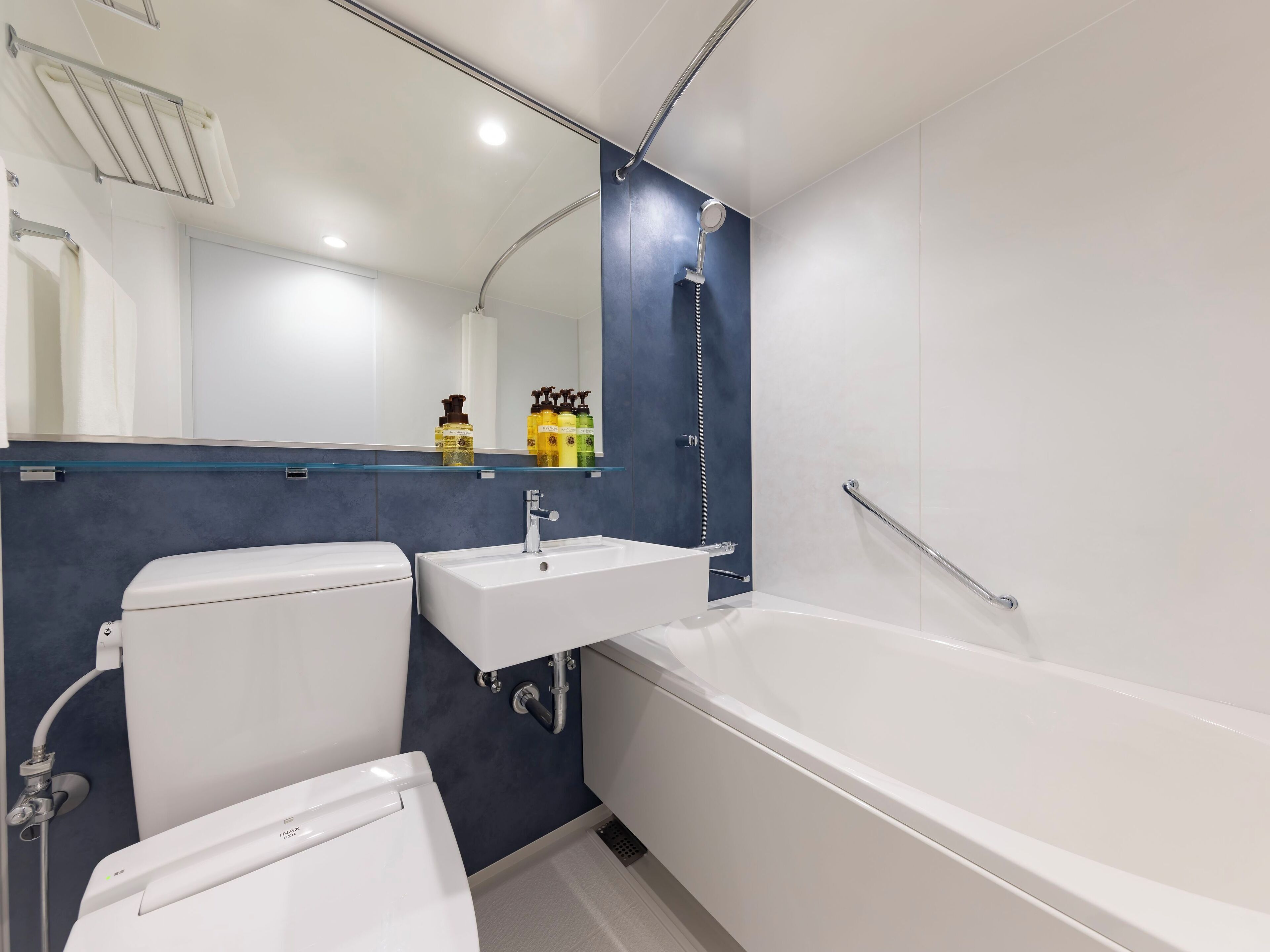 A modern bathroom with a white toilet, a sink, and a bathtub. There is a mirror above the sink and a showerhead above the bathtub.
