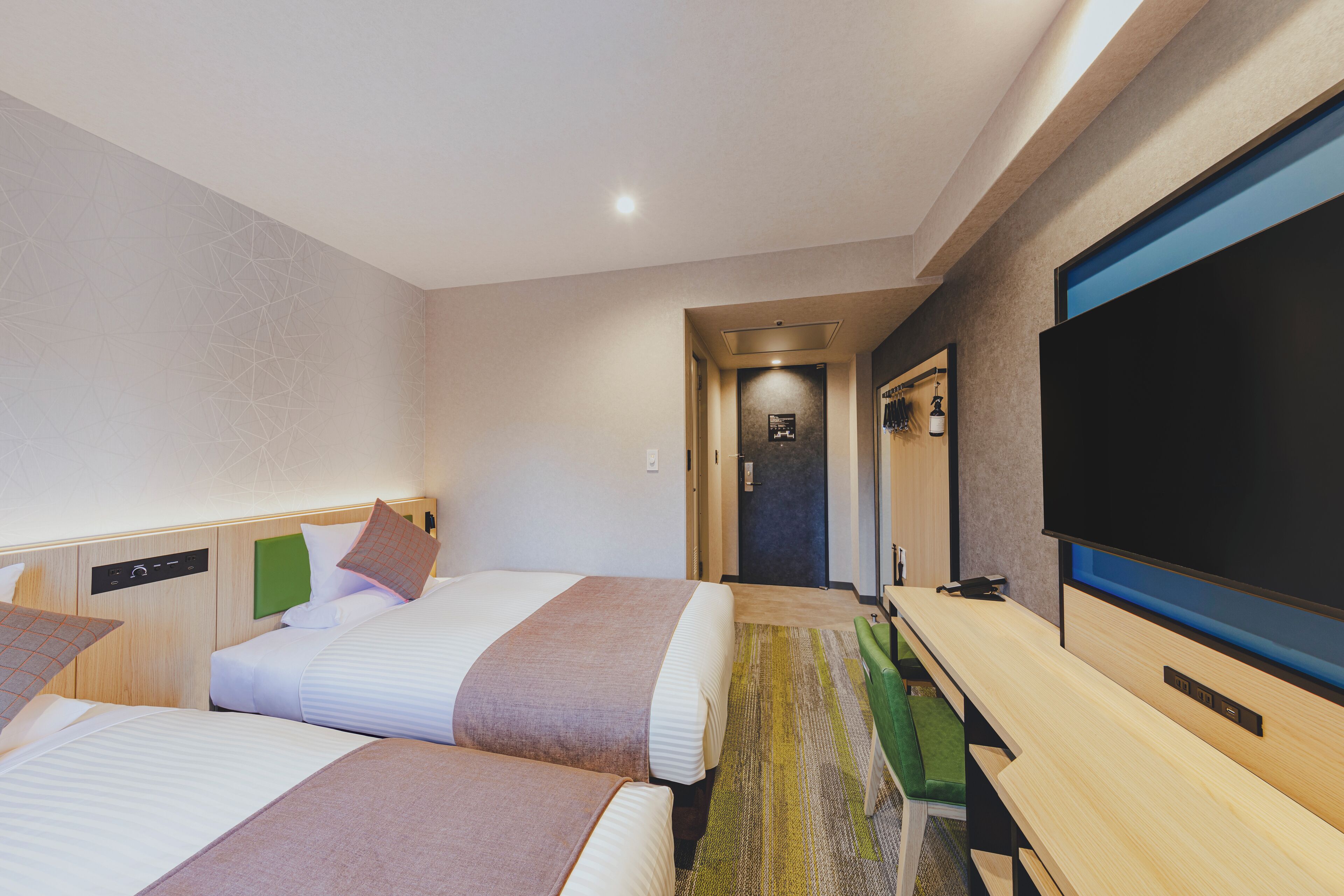 Habitación de hotel con dos camas, un televisor de pantalla plana, un escritorio y un sofá verde.