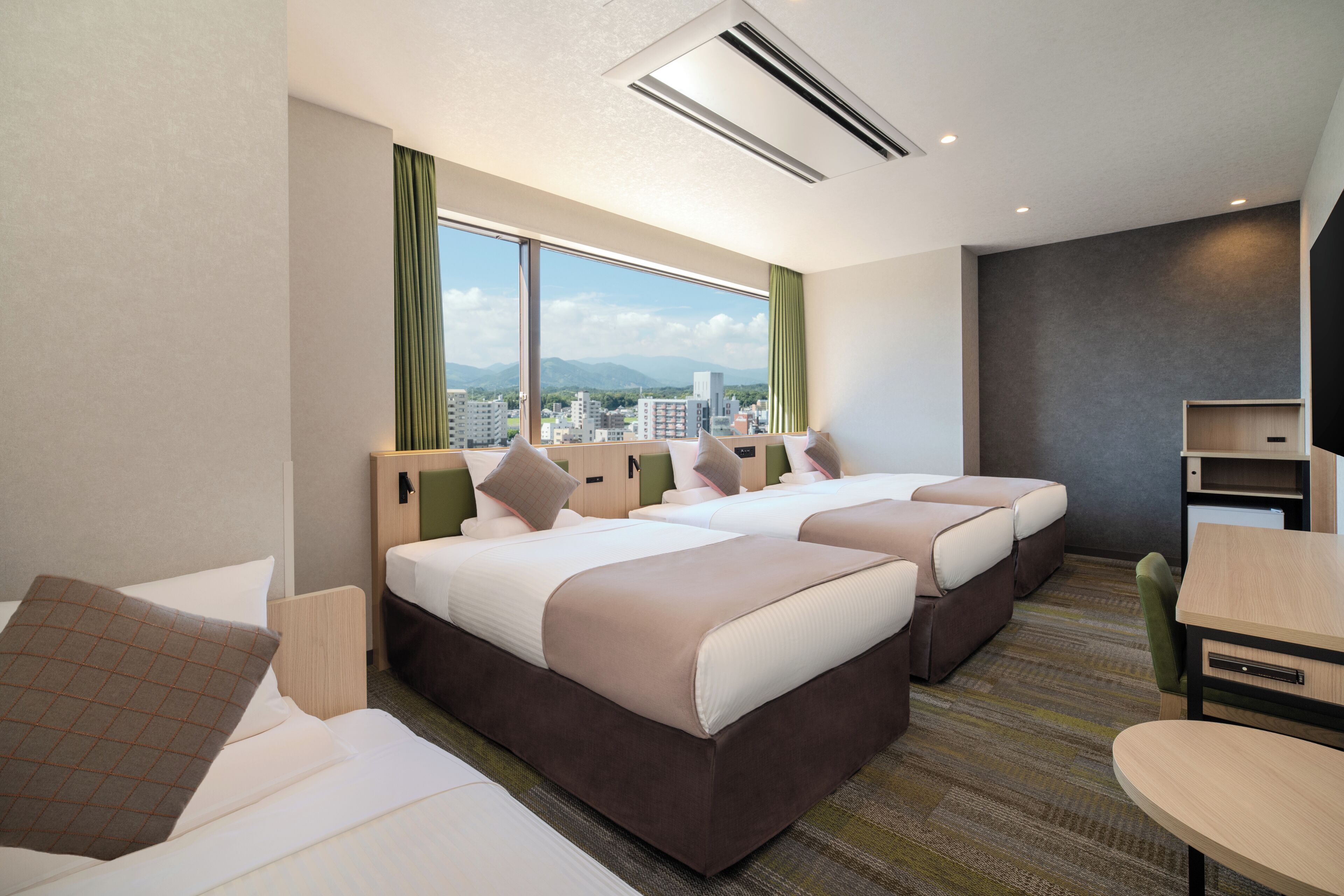 A hotel room with two beds, a desk, and a view of the city.