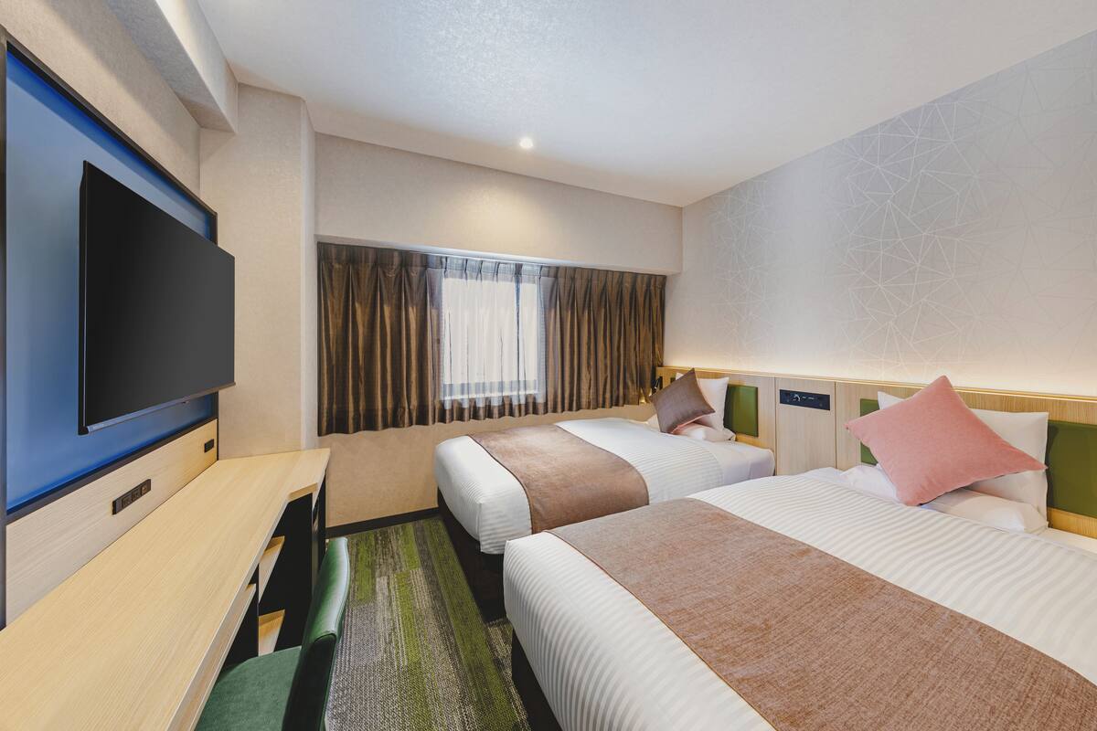 Ett hotellrum med två sängar, en platt-TV, ett skrivbord och ett fönster med gardiner.
