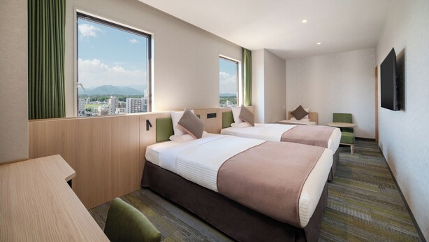 Quarto de hotel com duas camas, uma escrivaninha, uma cadeira e uma televisão.