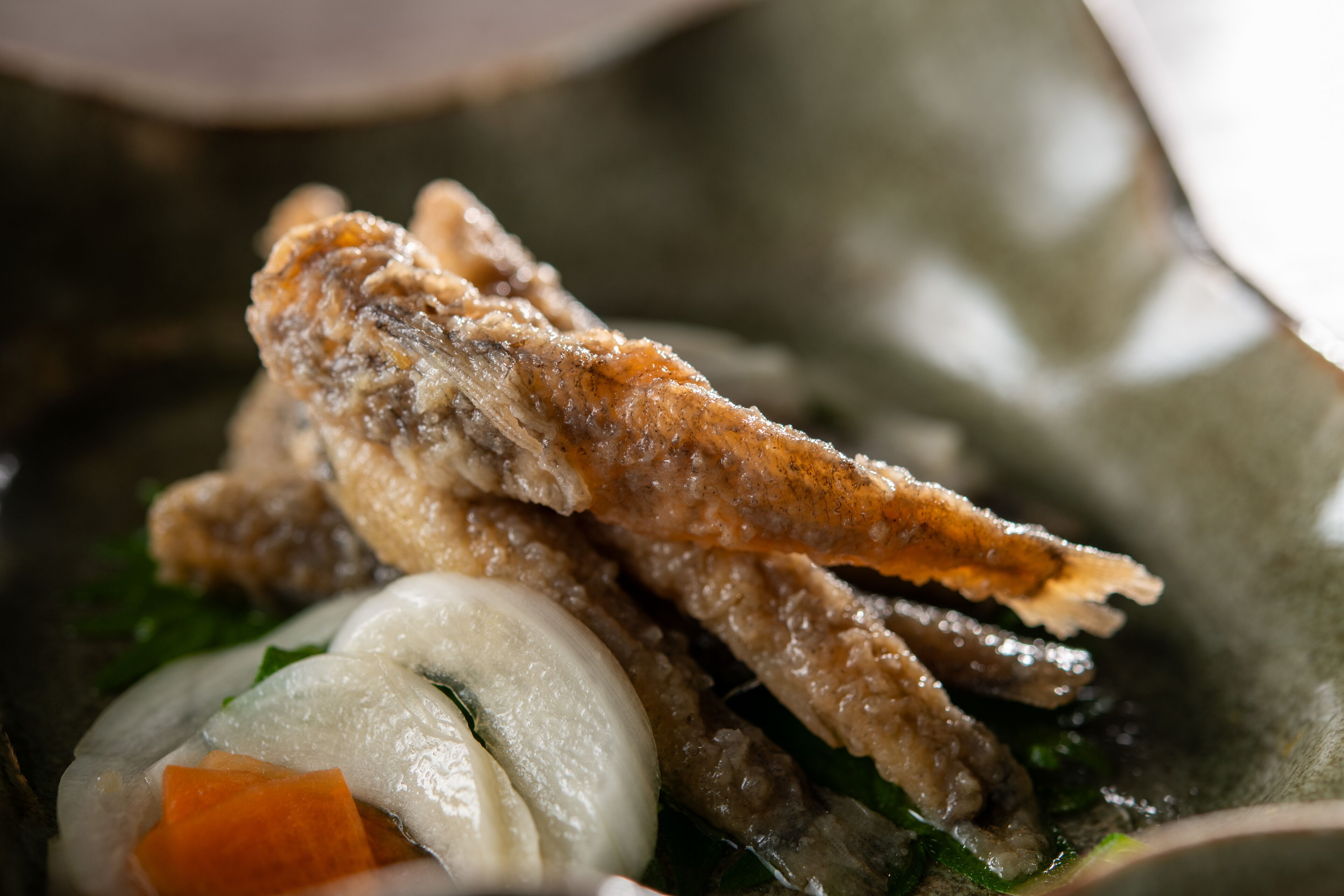 A close-up of a dish with fried items, possibly fish, alongside vegetables and a white spherical object, likely a dumpling.
