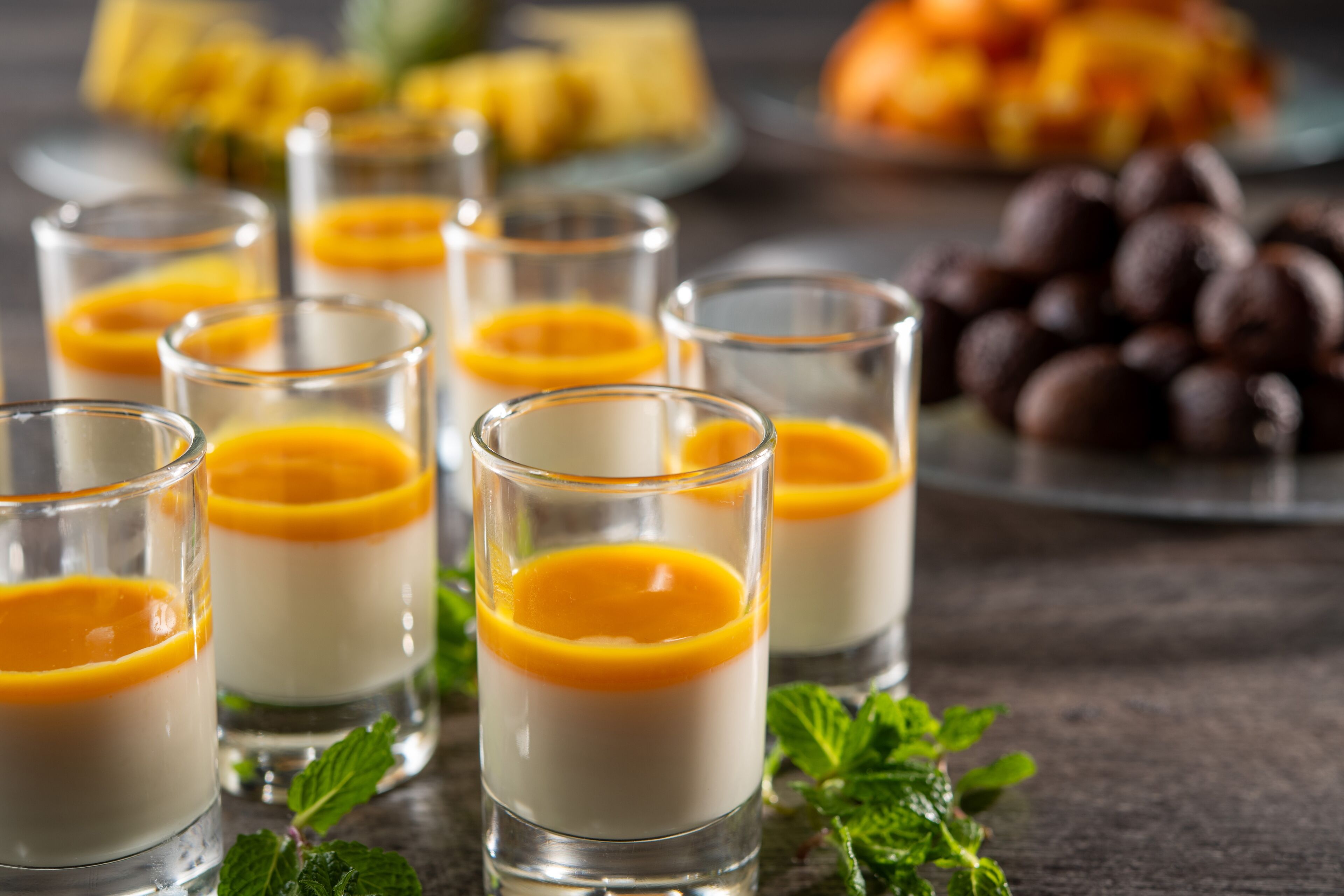 De petits verres remplis d’un dessert en couches, décorés de tranches d’orange et entourés de feuilles de menthe.