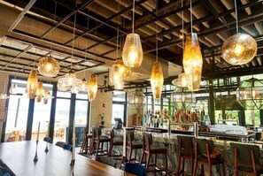 A restaurant with hanging pendant lights, a bar area with bottles, and a seating arrangement with tables and chairs.