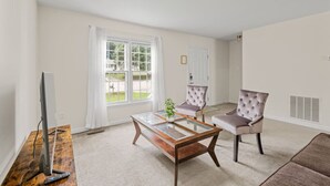A living room with a glass coffee table, two armchairs, a television, and a window with curtains. - * Prime Location: 2-BR Oasis with Washer & Dryer * (Richmond)