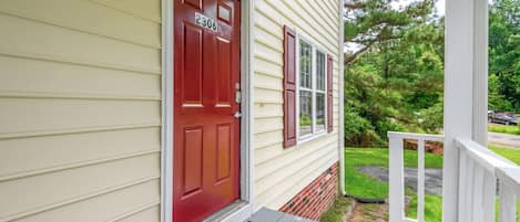 A house with a red door, number 2306, a porch with a white railing, and a green lawn.