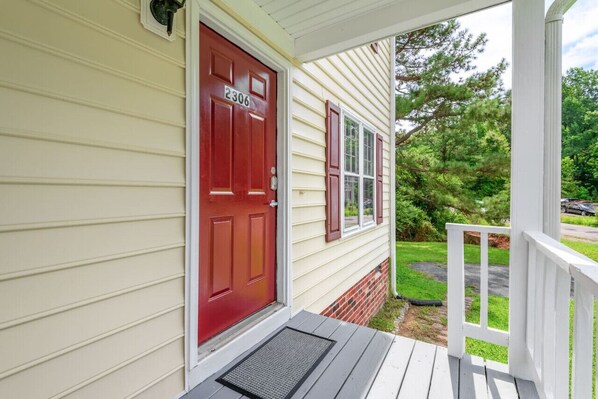 A house with a red door, number 2306, a porch with a white railing, and a green lawn.