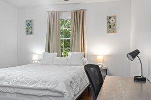 Ein Schlafzimmer mit einem Bett, zwei Nachttischlampen, einem Schreibtisch mit Lampe sowie zwei gerahmten Blumenbildern an den Wänden.