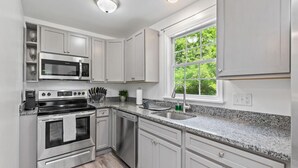 A modern kitchen with stainless steel appliances, white cabinetry, a granite countertop, and a window with a view of greenery. - $ Cozy 1BR 1BA Apartment: Near Fort Gregg-Adams $ (Hopewell)