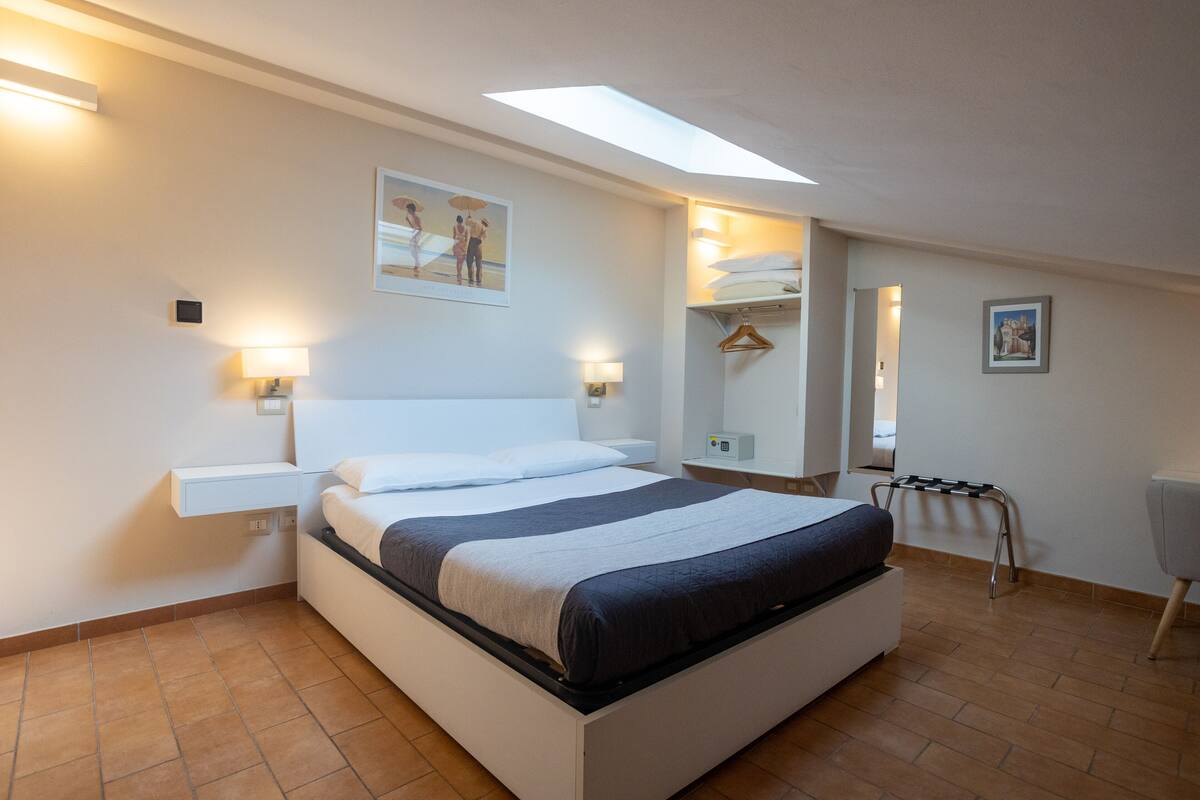 A modern bedroom with a bed, bedside lamps, a ceiling light, a wardrobe, and a mirror.