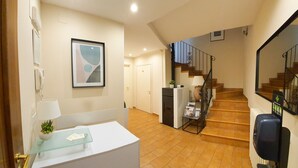 A hallway with a reception desk, a staircase, and a wall-mounted mirror. - Helios Assisi (Assisi)