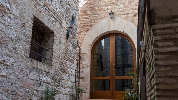 A stone building with a wooden door and steps leading to a courtyard. - Helios Assisi (Assisi)