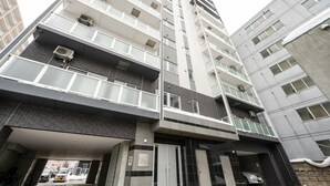 Un edificio de varios pisos con balcones, un acceso cubierto y un estacionamiento.