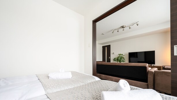 Habitación de hotel con dos camas, un espejo grande, un televisor de pantalla plana y un rincón de descanso con una planta.