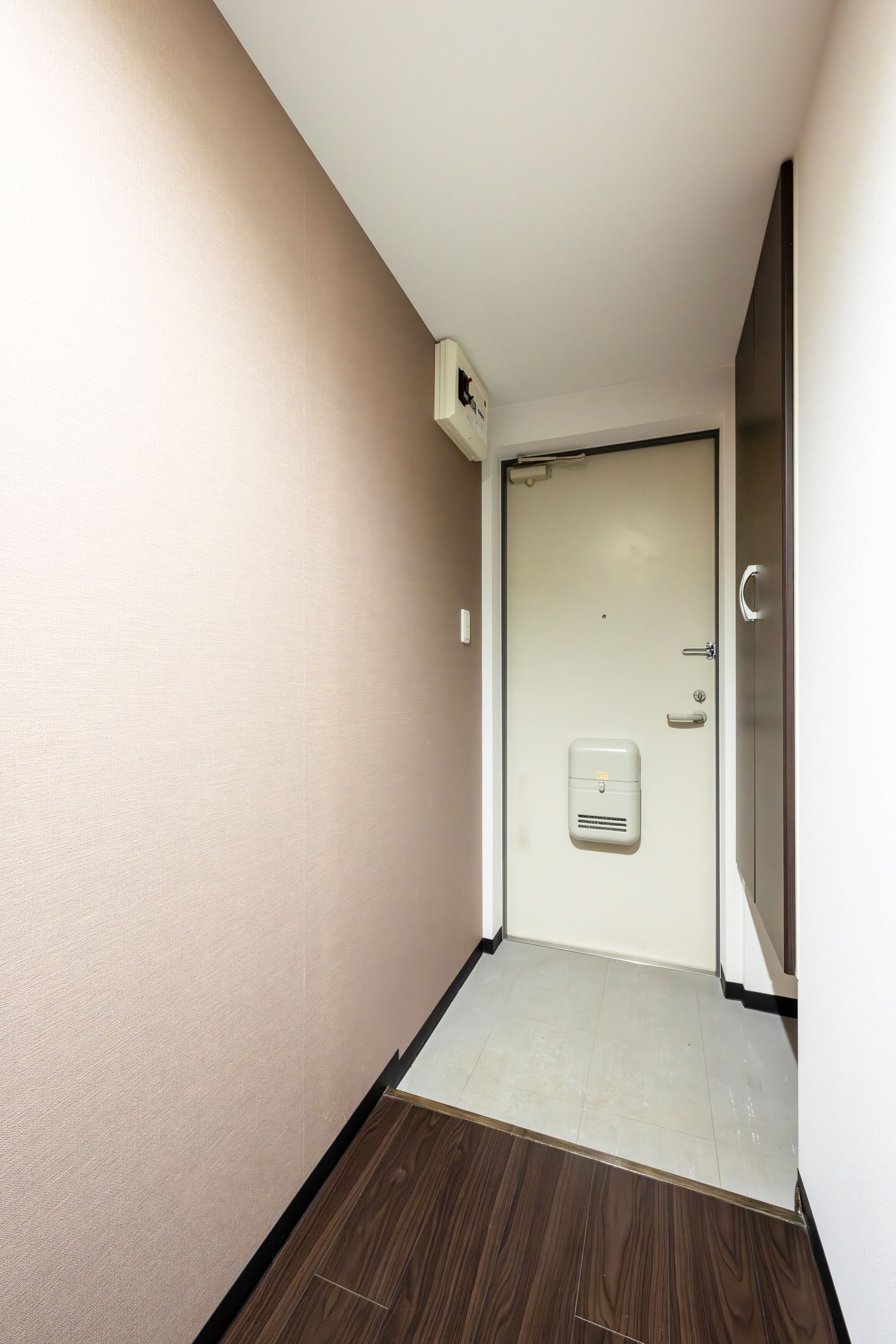 A narrow hallway with a door at the end, a small air conditioning unit mounted on the wall, and a wooden floor.