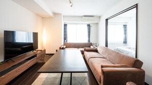Una sala de estar moderna con un televisor de pantalla plana, un sofá, una mesa de centro y un gran ventanal con cortinas.