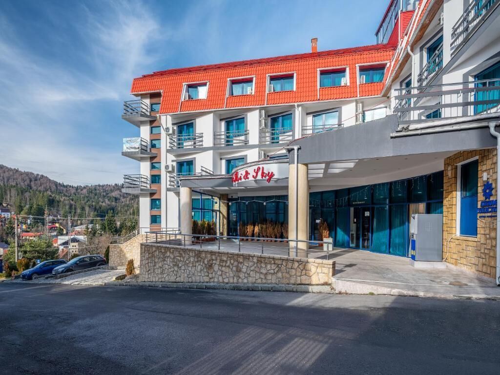 A modern hotel with a red roof, multiple balconies, and a covered entrance.