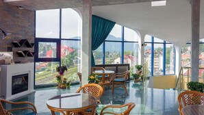 A spacious room with a large window offering a view of the cityscape. There is a fireplace, wicker furniture, and potted plants. - Hotel Ski & Sky (Predeal)