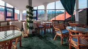 A restaurant with wicker furniture, glass tables, and large windows offering mountain views. - Hotel Ski & Sky (Predeal)