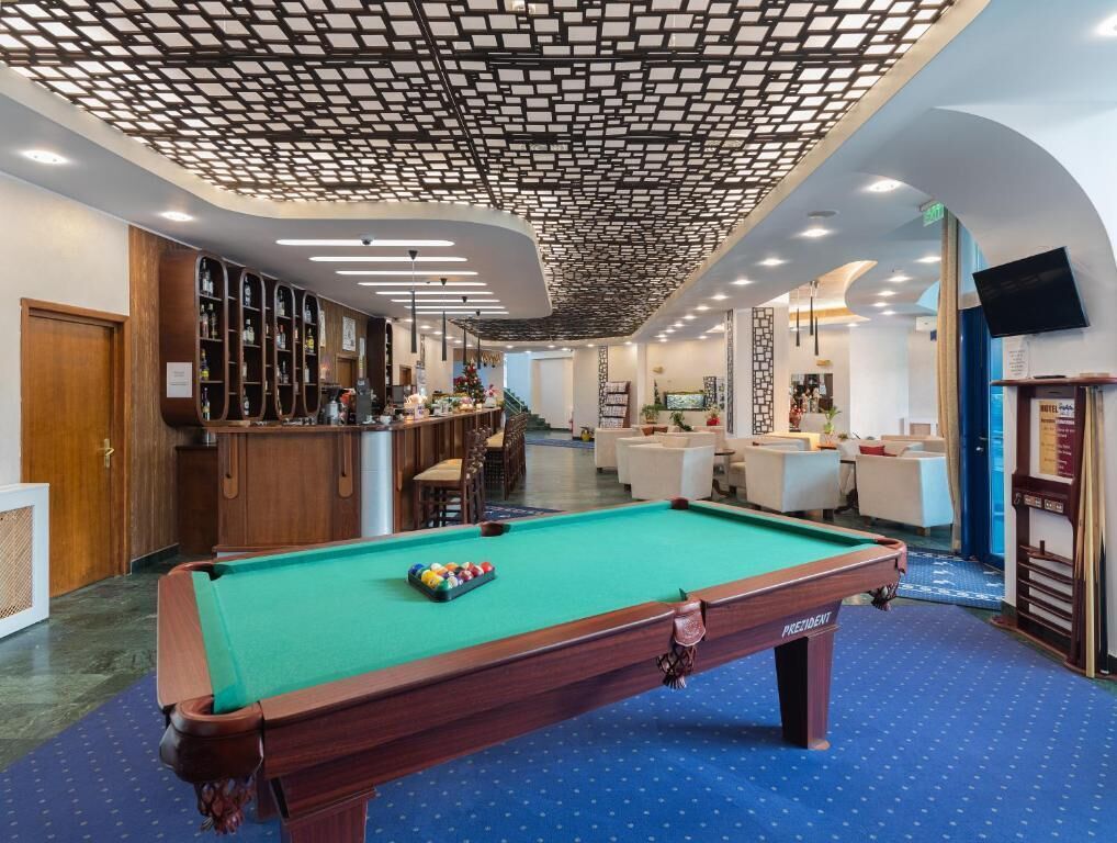 A pool table in a hotel lobby with a bar area and seating.