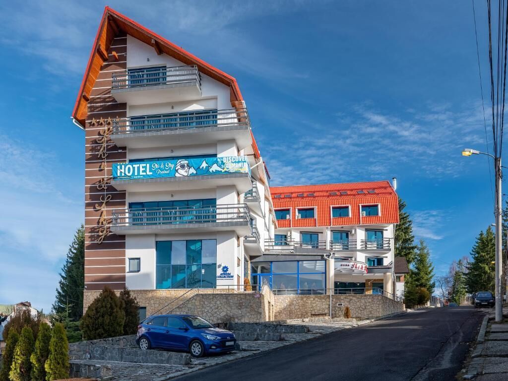 A multi-story hotel with balconies, a ski resort sign, and a red-roofed building in the background.