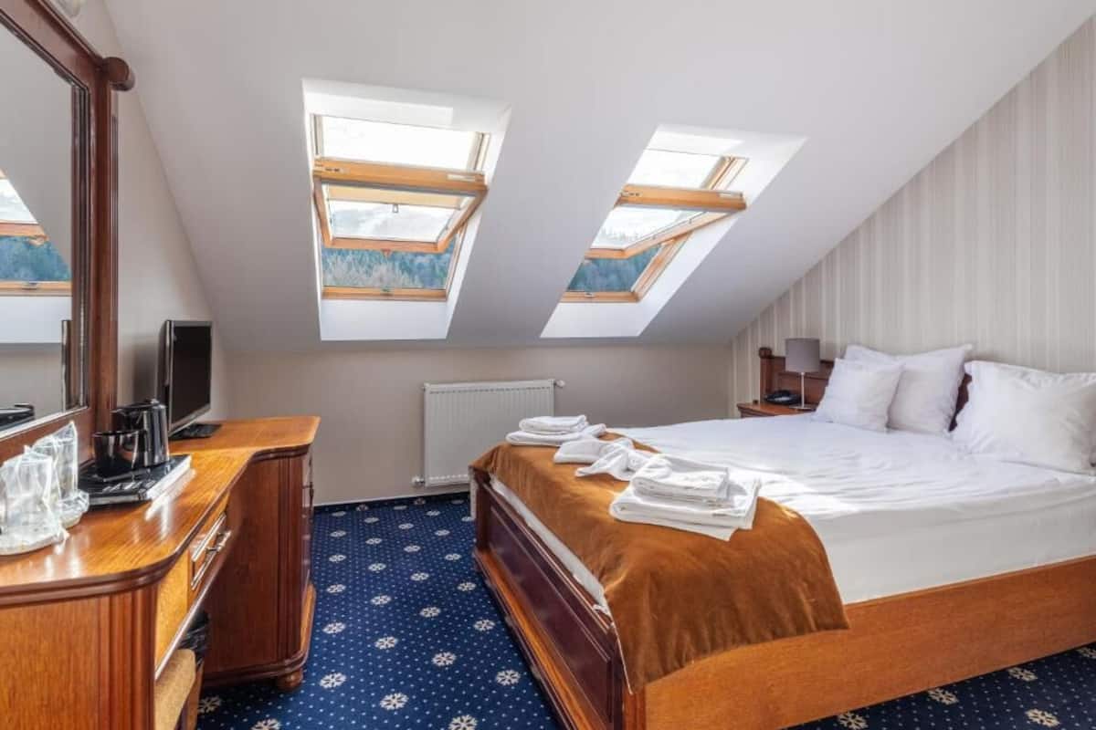 A hotel room with a large bed, a desk with a mirror, and two skylights.