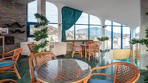 A modern lounge area with wicker furniture, a glass table, and large windows offering a mountain view. - Hotel Ski & Sky (Predeal)