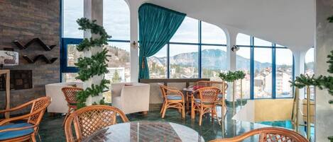 A modern lounge area with wicker furniture, a glass table, and large windows offering a mountain view.