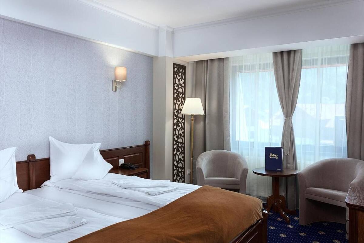 A hotel room with a neatly made bed, two armchairs, a small table, and a decorative partition.