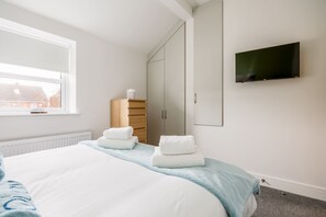 Ein Hotelzimmer mit Bett, Wandfernseher, Fenster mit Blick auf Gebäude und Kleiderschrank.