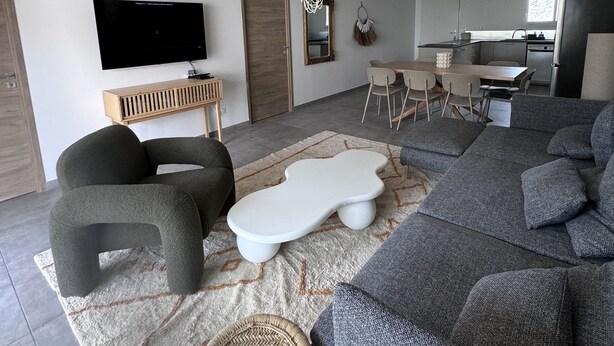 A modern living room with a large grey sectional sofa, a white coffee table, and a television on a wooden stand.