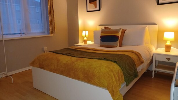 Een keurig opgemaakte slaapkamer met een bed, nachtlampjes en een raam met gordijnen.