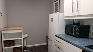 Een kleine keuken met witte kastjes, een groene magnetron en een houten tafeltje.