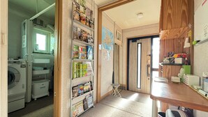 A laundry area with a washing machine, a drying rack, and a shelf with various items. - Guest House MOMO (Obihiro)