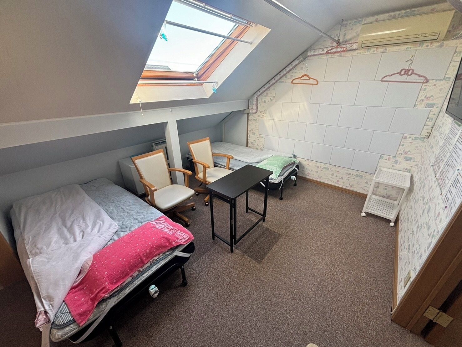 Habitación de residencia con tragaluz, dos camas individuales, un escritorio, dos sillas y un radiador.