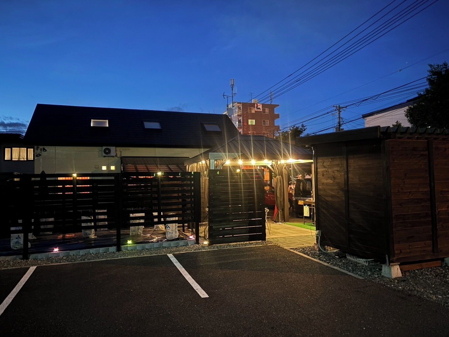 A building with a gated entrance, a parking area, and a small adjacent structure.