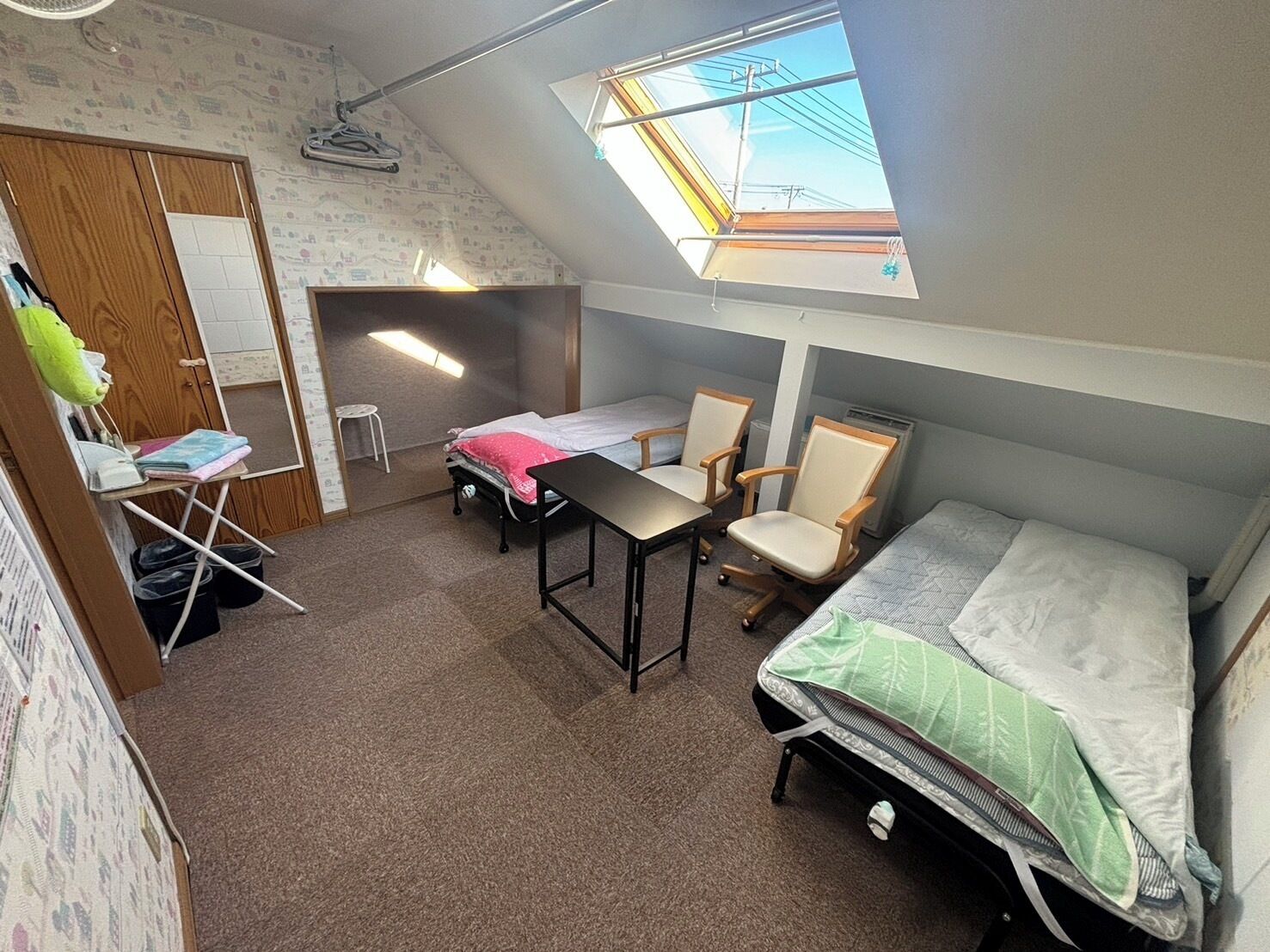 A compact dormitory room with a skylight, a bed, a desk, and two chairs.