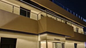 A building with a flat facade, a visible storefront with a sign, and a balcony with plants.