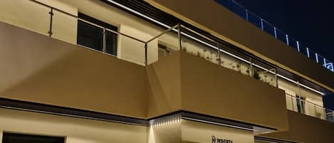 A building with a flat facade, a visible storefront with a sign, and a balcony with plants.