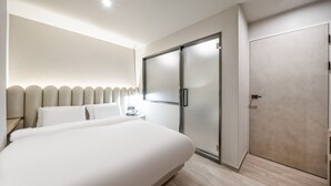 A modern hotel room with a large bed, a wardrobe, and a bedside table.