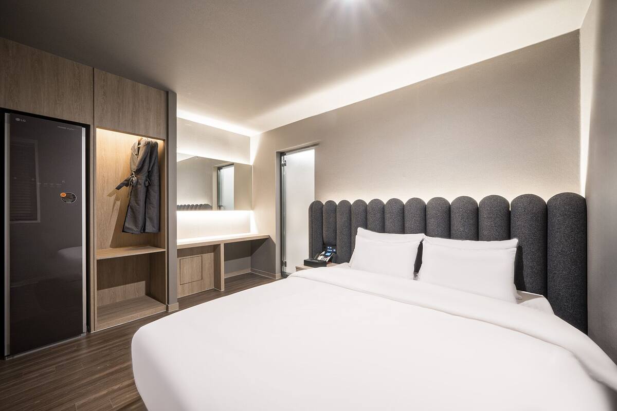 Een moderne hotelkamer met een groot bed, een houten garderobe, een kaptafel met spiegel en een nachtkastje met telefoon.