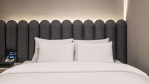 A neatly made bed with white linens and pillows, a modern headboard with a textured pattern, and a bedside table with a phone.