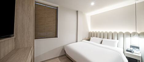 Una habitación de hotel moderna con una cama grande, un televisor montado en un panel de madera, una mesita de noche con una lámpara y una ventana con persianas.