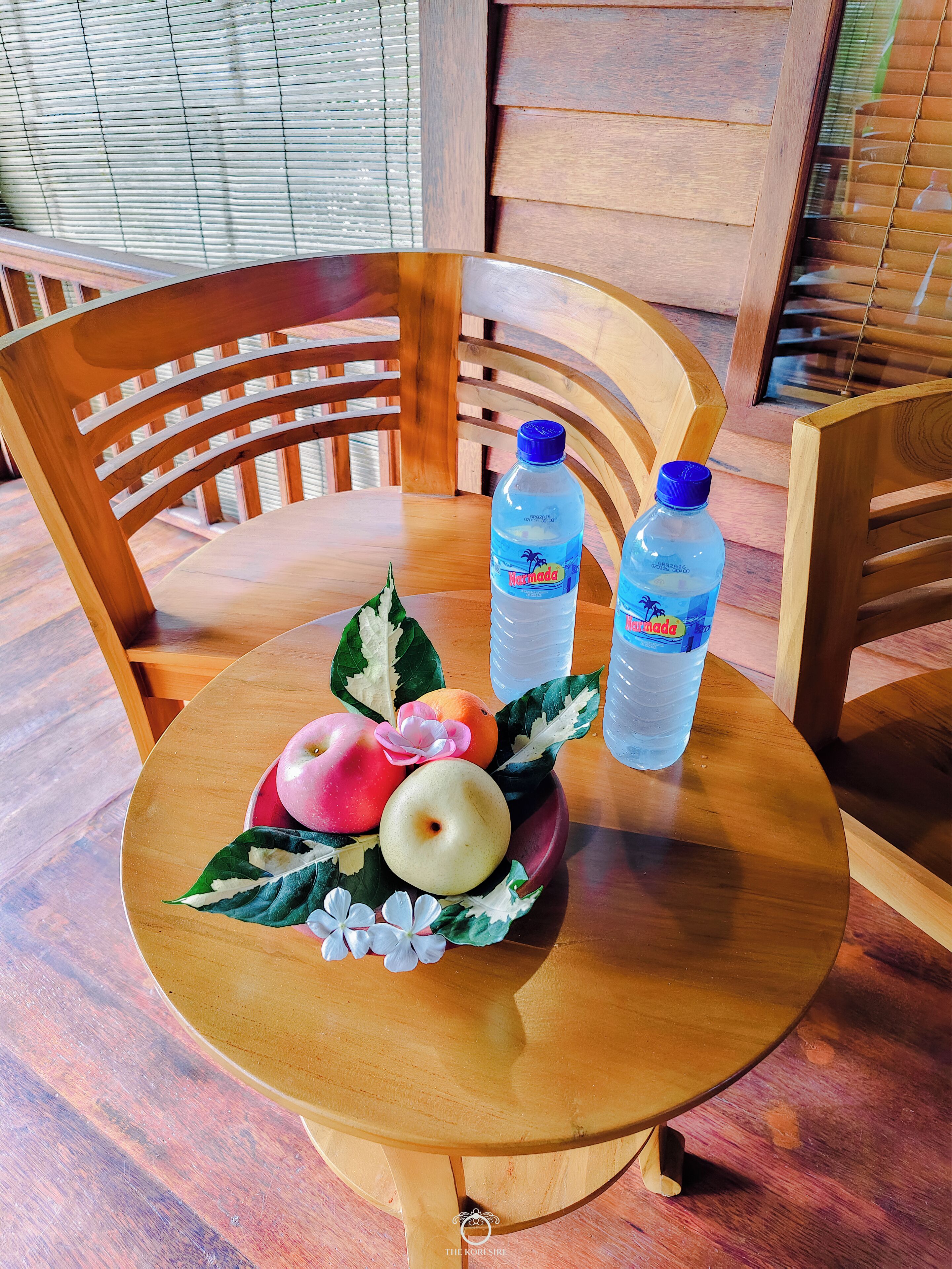 A round wooden table with two bottles of water, a bowl of fruit, and decorative leaves.