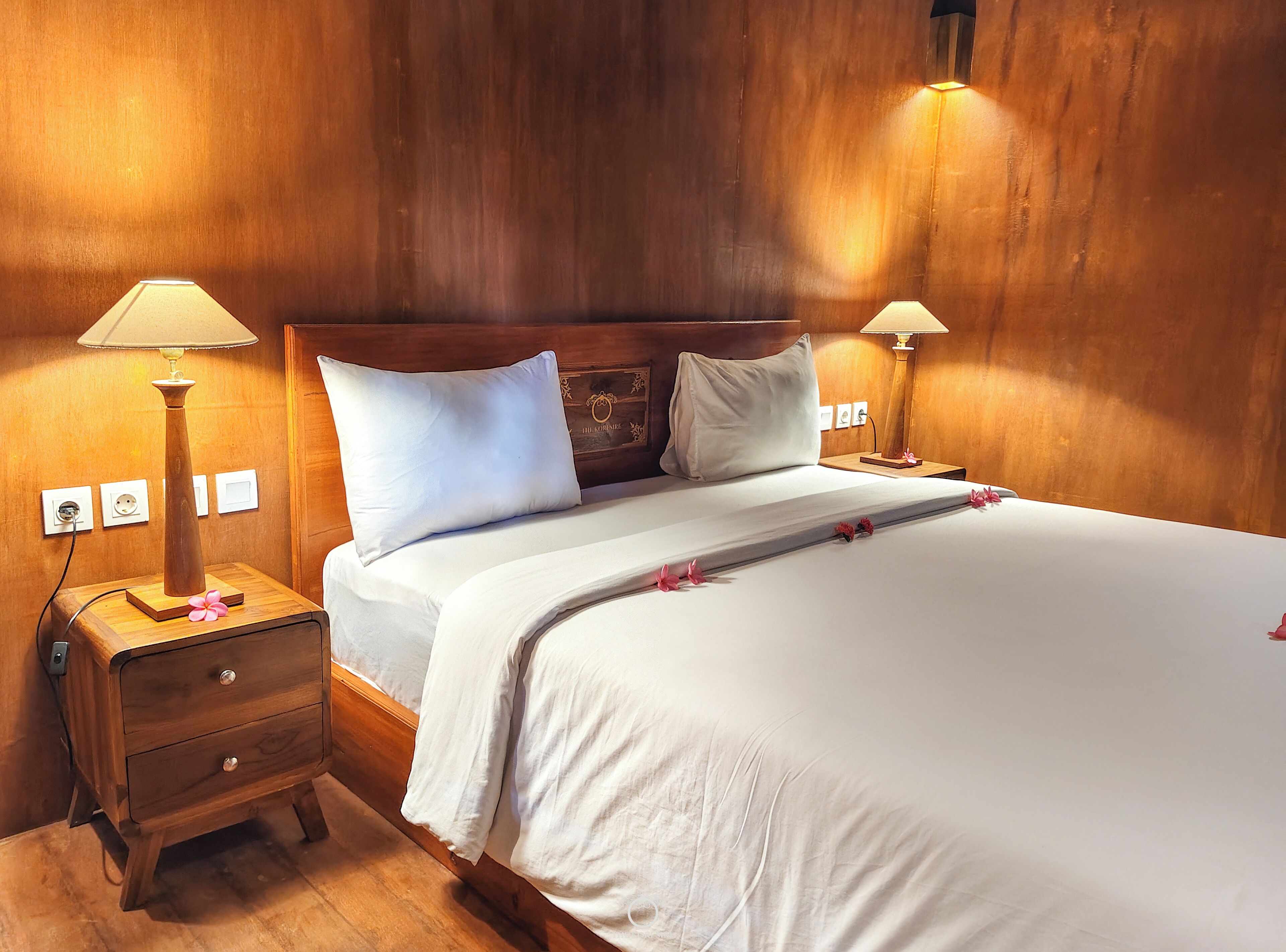 A neatly made bed with white linens, two bedside lamps, and a wooden nightstand with a drawer.