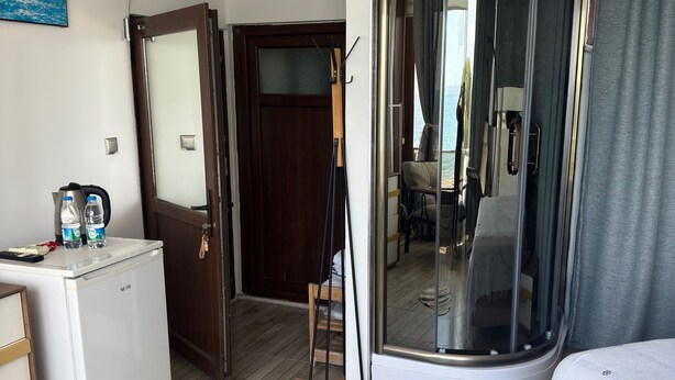 A room with a white refrigerator, a wooden chair, a glass door leading outside, and a bed with a white cover. - Ellawilla Suit House (Edremit)