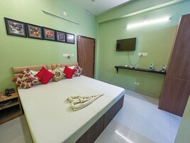 Un dormitorio con cama, almohadas, televisor, repisa con botellas e imágenes enmarcadas en la pared.