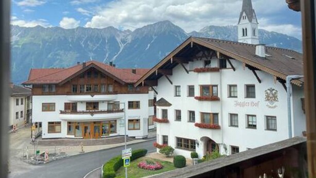 A hotel with a traditional Alpine architectural style, featuring a prominent church steeple in the background. - Apartment mit Bergblick (Aldrans)